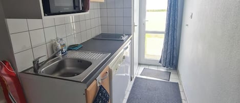Pieni, käytännöllinen keittiö, jossa on mikroaaltouuni, pesuallas ja puukehikoiset kaapit.