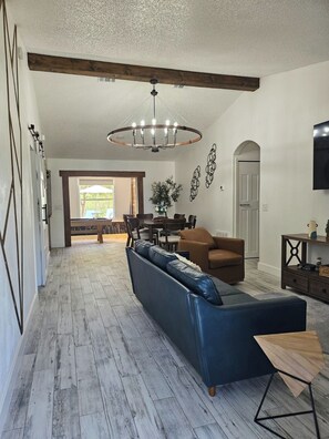 Ein geräumiges Wohnzimmer mit einem großen, blauen Sofa, einem Holzessttisch und einer Kronleuchter.