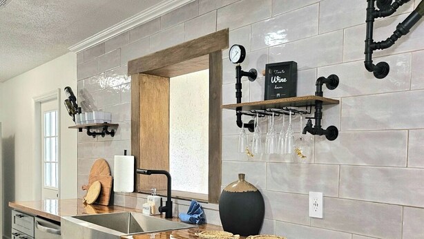 Una cucina moderna con mobili grigi, un piano di lavoro in legno, un lavello incassato e uno schienale con una sveglia e una dispensa per vino.