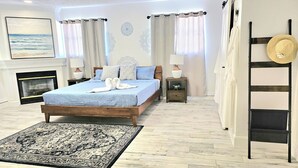 Una camera da letto con un letto, un camino, un comodino, una lampada, un cappello su un appendiabiti e un tappeto.
