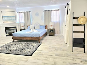 Ein Schlafzimmer mit einem Bett, einem Kamin, einem Nachttisch, einer Lampe und einem Hut auf einem Wäscheständer.