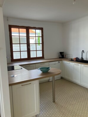 Eine Küche mit Fenster, weißen Schränken, einer Spüle und einer türkisblauen Schüssel auf der Arbeitsfläche.