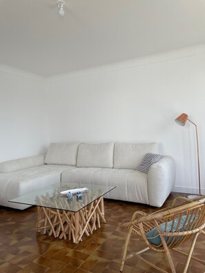 Ein modernes Wohnzimmer mit einem Glastisch, einem weißen Sofa, einer Stehlampe und einem Korbstuhl.