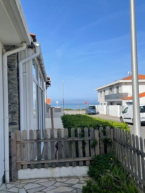Eine Wohnstraße mit einer Steinmauer, einem Holzzaun und freiem Blick auf das Meer.