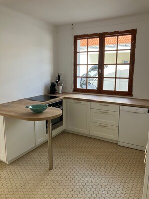 Eine Küche mit weißen Schränken, einer Holz Arbeitsplatte, einem runden Tisch und einem Fenster mit Blick auf ein Gebäude.