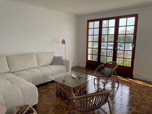 Ein Wohnzimmer mit einer Couch, einem Glastisch, Korbstühlen und einem großen Fenster mit Blick.