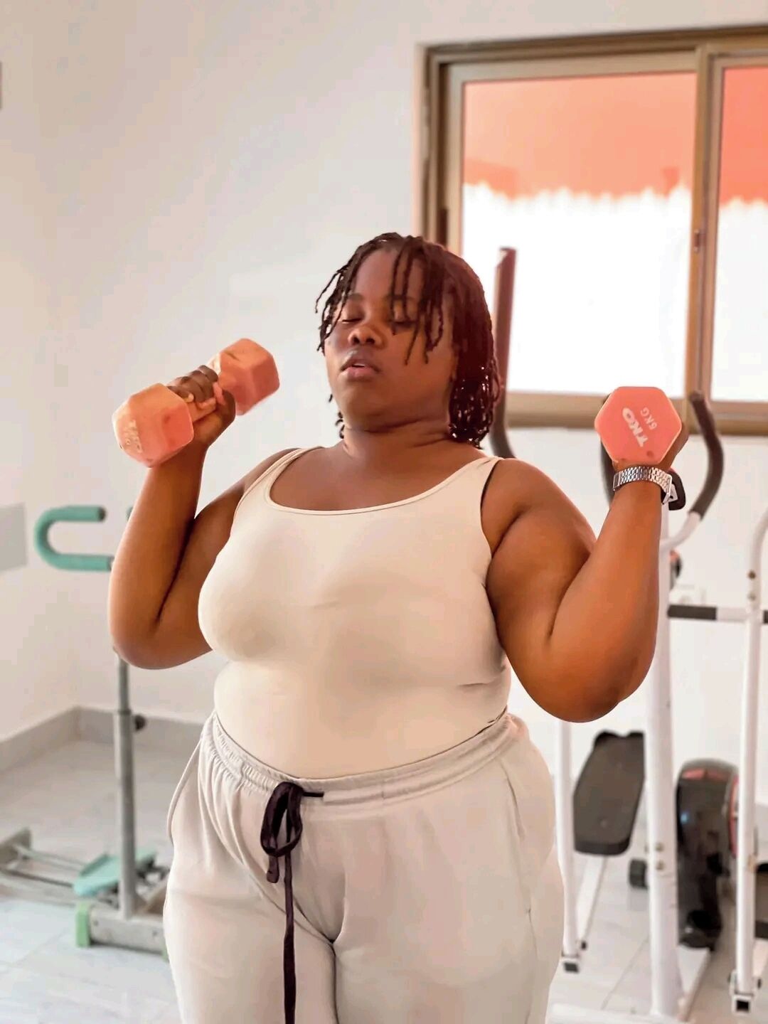 Une personne s’entraîne avec des haltères dans une salle de sport, avec d’autres équipements d’exercice en arrière-plan.