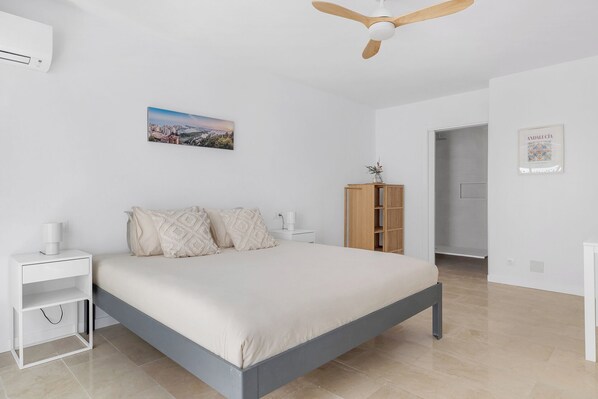 Een slaapkamer met een bed, nachtkastjes, een plafondventilator, een houten kast en een ingelijst schilderij aan de muur.