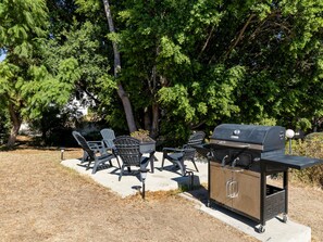 Een terras buiten met een barbecue en stoelen.