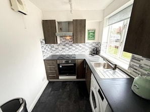 A modern kitchen with dark wood cabinets, a tiled backsplash, a built-in oven, a sink, and a window. - 1 bed - Sleeps 4 - Free Parking & Wifi (Redhill)