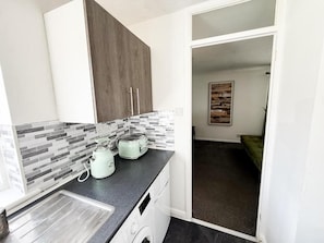 Eine Küche mit Toaster, Wasserkocher und Waschmaschine, einer gefliesten Spritzschutzeinrichtung und einem Holzkasten.