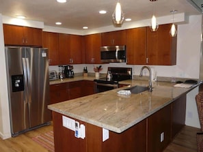 A modern kitchen with wooden cabinets, stainless steel appliances, and a granite countertop. - Ocean View 2BR Loft Near Napili Beach - Unit C34 (Lahaina)