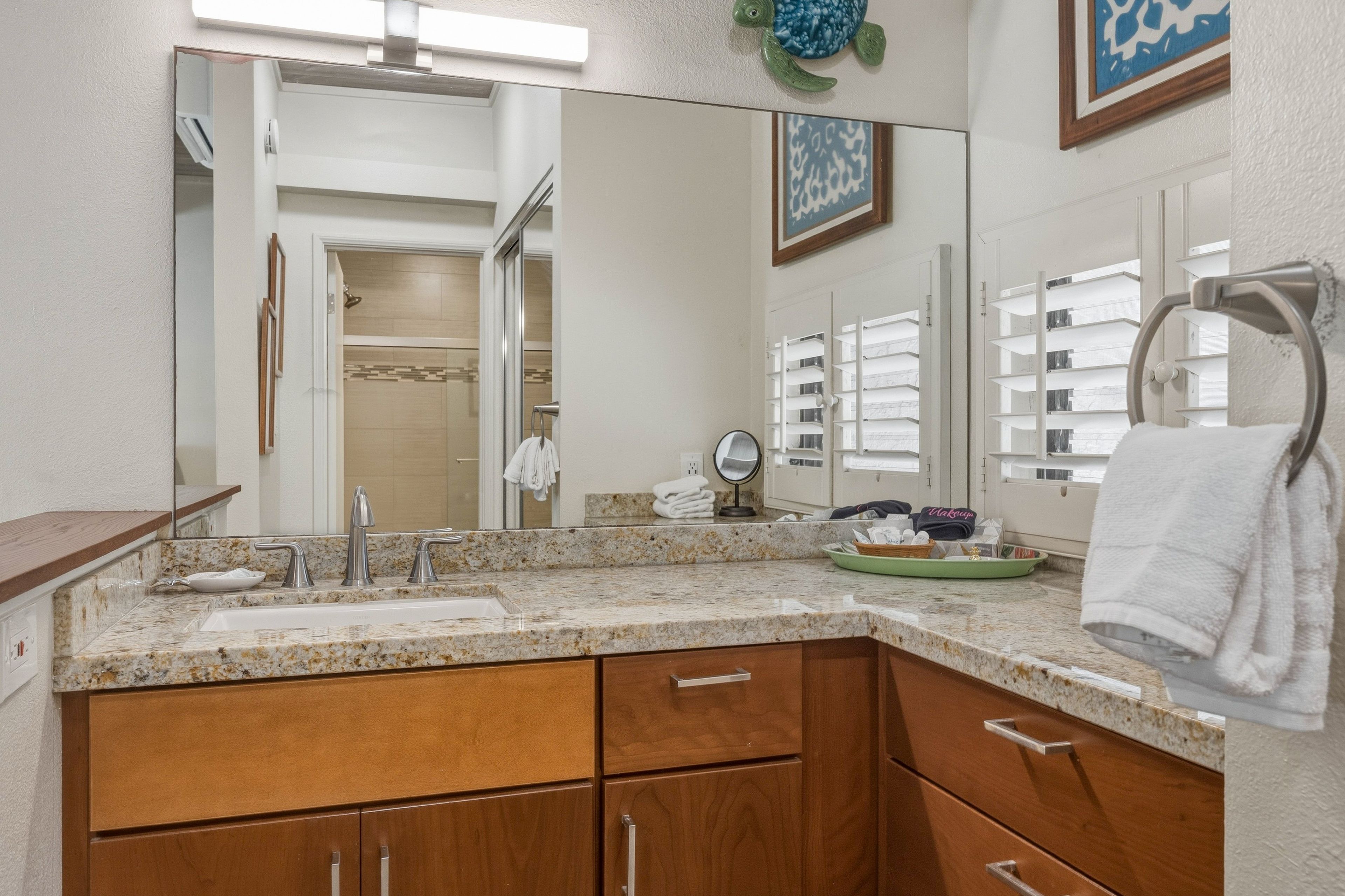 A bathroom with a granite countertop, wooden cabinets, a mirror, and a towel rack.