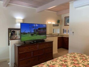 A room with a television on a wooden dresser, a bed with a floral bedspread, a kitchen area with a refrigerator, and a bathroom with a shower. - Ocean View 2BR Loft Near Napili Beach - Unit C34 (Lahaina)