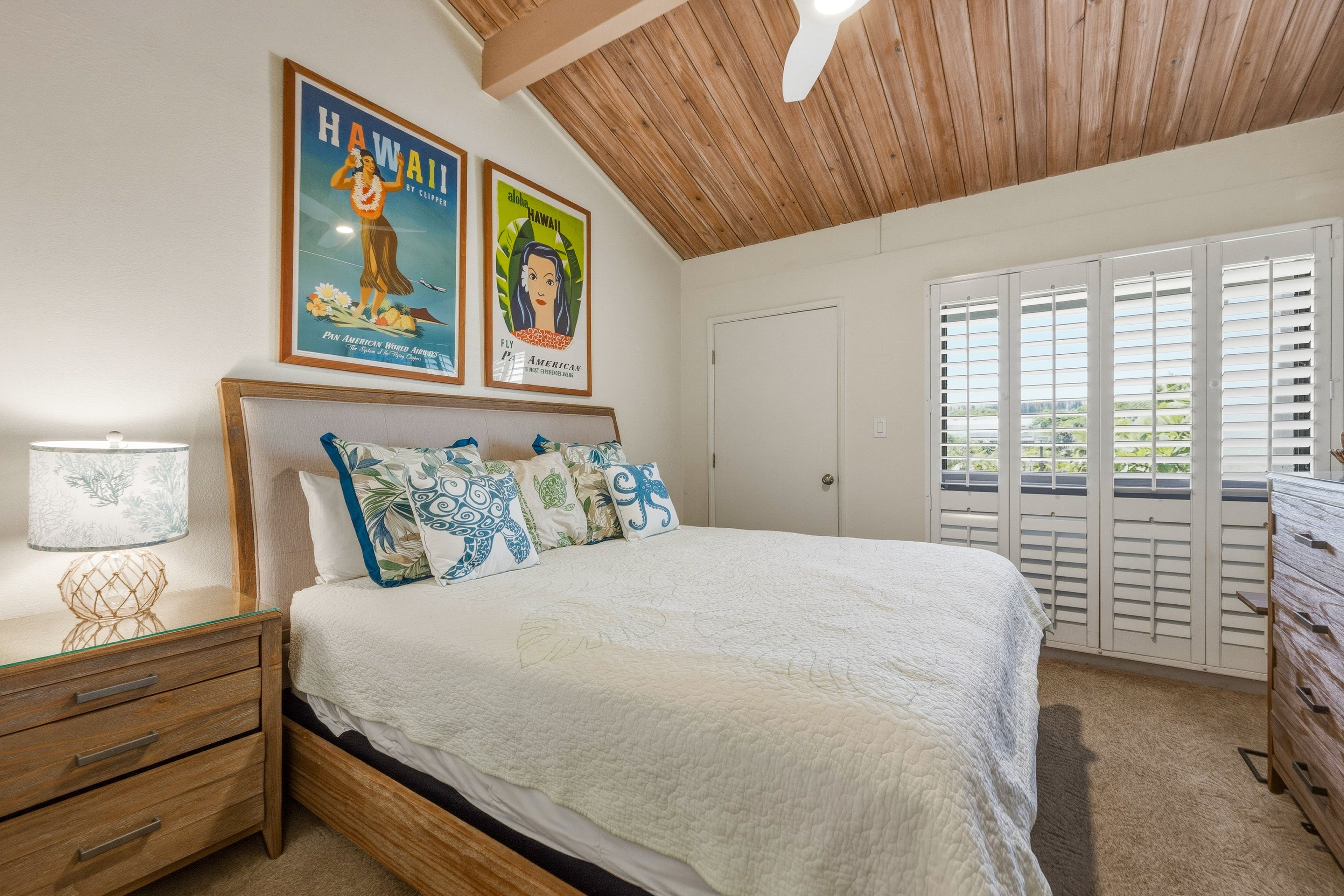 A bedroom with a bed, a nightstand, a lamp, a wooden ceiling, and two posters on the wall.