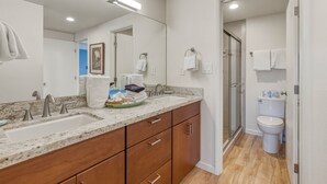 A modern bathroom with a double sink vanity, a glass shower enclosure, and a toilet. - Ocean View 2BR Loft Near Napili Beach - Unit C34 (Lahaina)