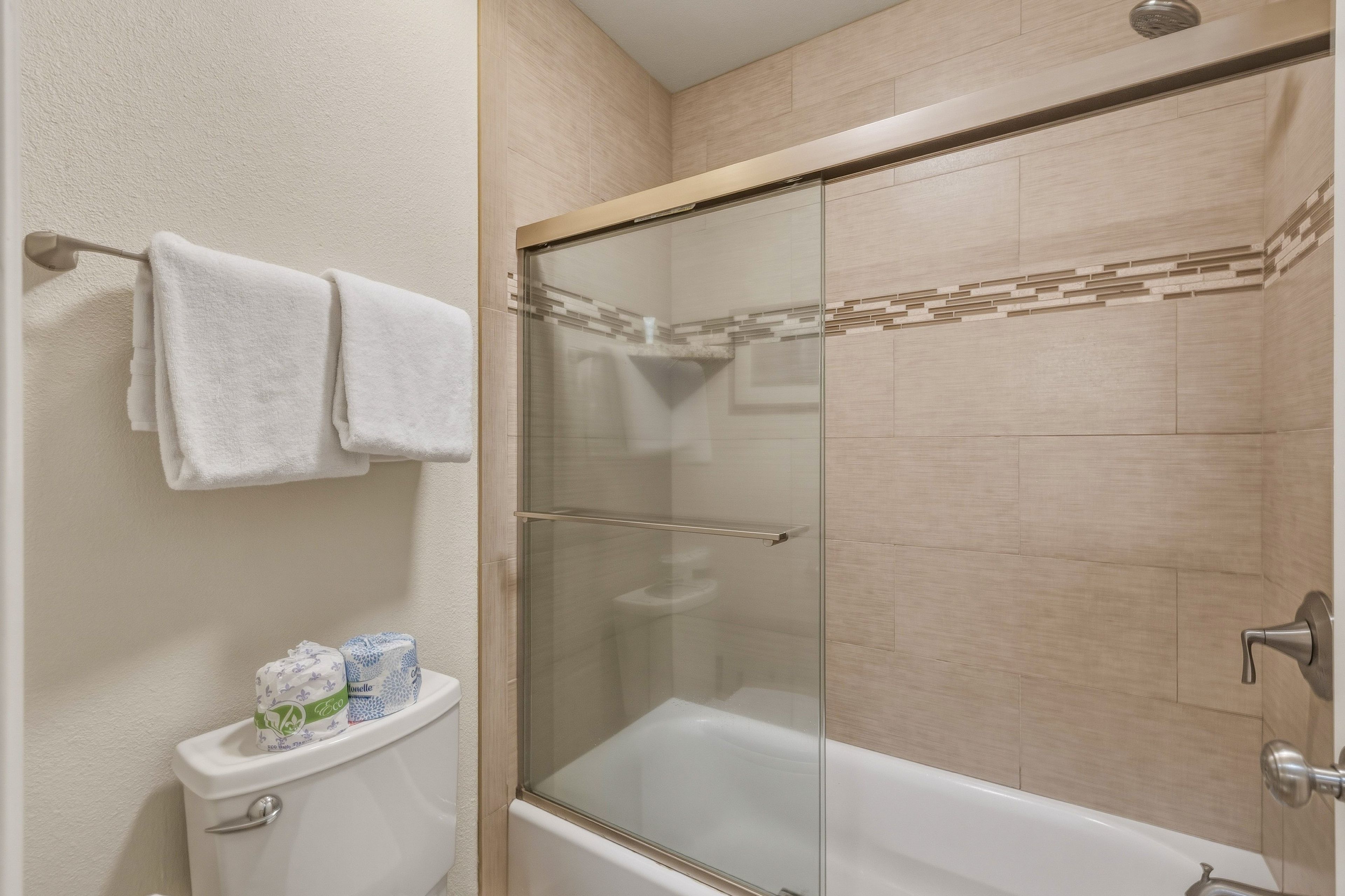 A bathroom with a toilet, a glass-enclosed shower, and a towel rack with two towels.