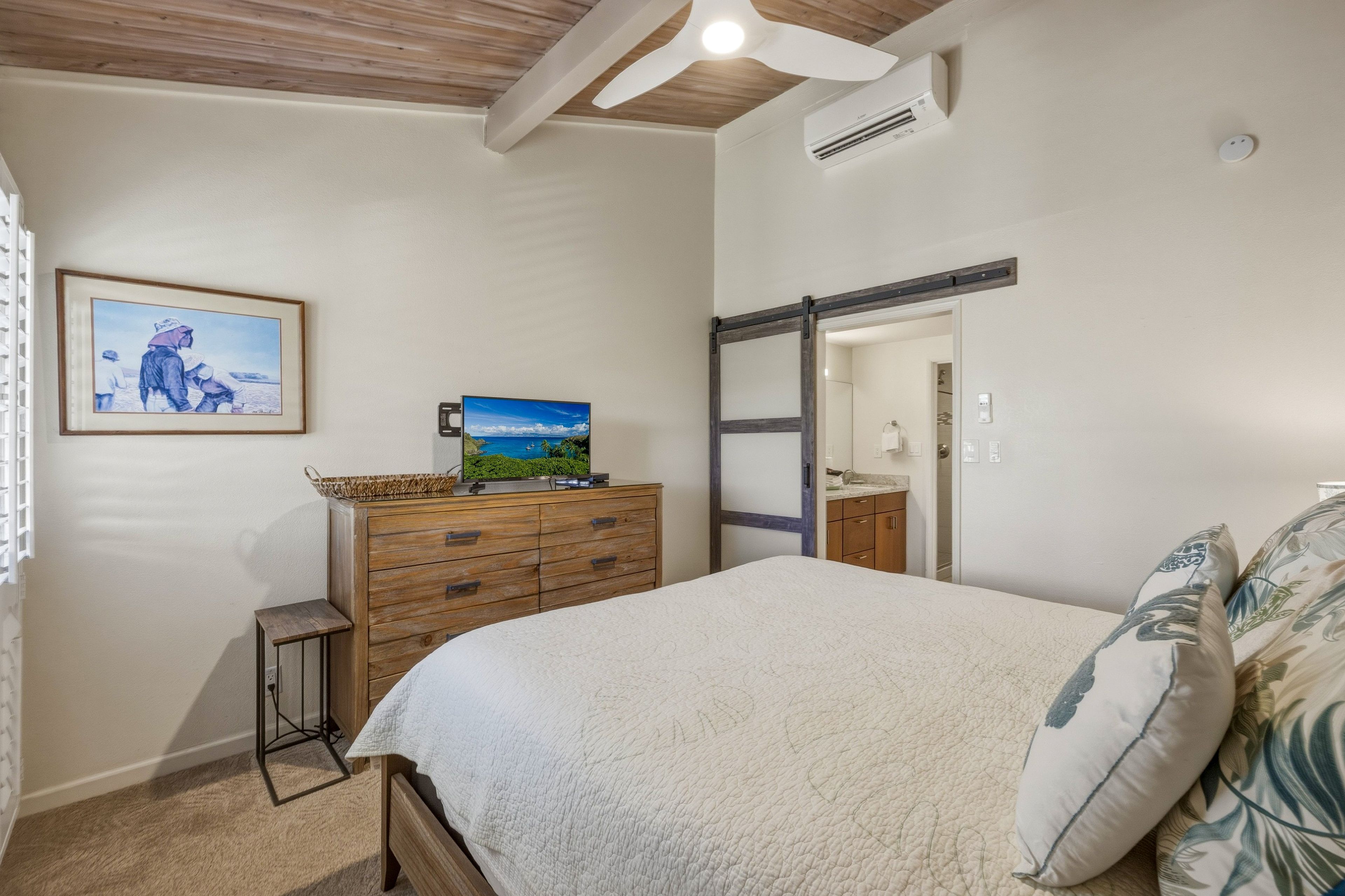 A bedroom with a bed, a dresser, a television, and a painting on the wall.
