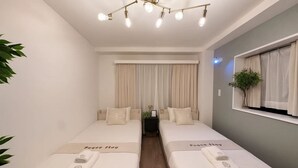 Ein Doppelzimmer mit zwei Betten, einer Deckenleuchte, einem Fenster mit Vorhängen und einer Zimmerpflanze.
