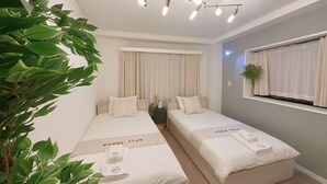 Ein Hotelzimmer mit zwei Betten, einer Deckenleuchte, einem Fenster mit Vorhängen und einer Pflanze.