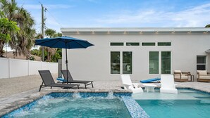 A swimming pool with lounge chairs and an umbrella, surrounded by a modern house with large windows and a white exterior. - Ringside On Ringling 4 Bedroom Home (Sarasota)