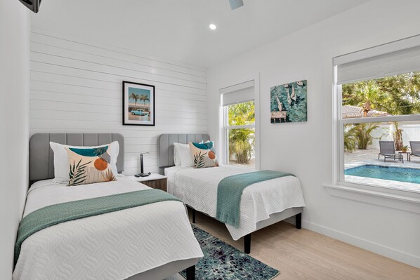 A bedroom with two beds, a window with a view of a swimming pool, and artwork on the walls. - Ringside On Ringling 4 Bedroom Home (Sarasota)
