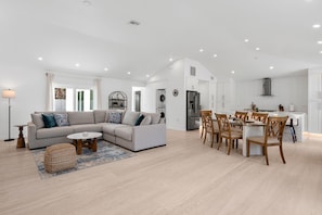 A modern living room with a sectional sofa, a dining table with chairs, a kitchen area with a refrigerator, and a laundry room. - Ringside On Ringling 4 Bedroom Home (Sarasota)