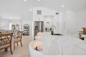A modern kitchen with white cabinetry, a marble island, and a built-in refrigerator. - Ringside On Ringling 4 Bedroom Home (Sarasota)