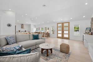 A spacious living area with a sofa, coffee table, and ottoman, a dining area with chairs, and a kitchen with cabinets and a countertop. - Ringside On Ringling 4 Bedroom Home (Sarasota)