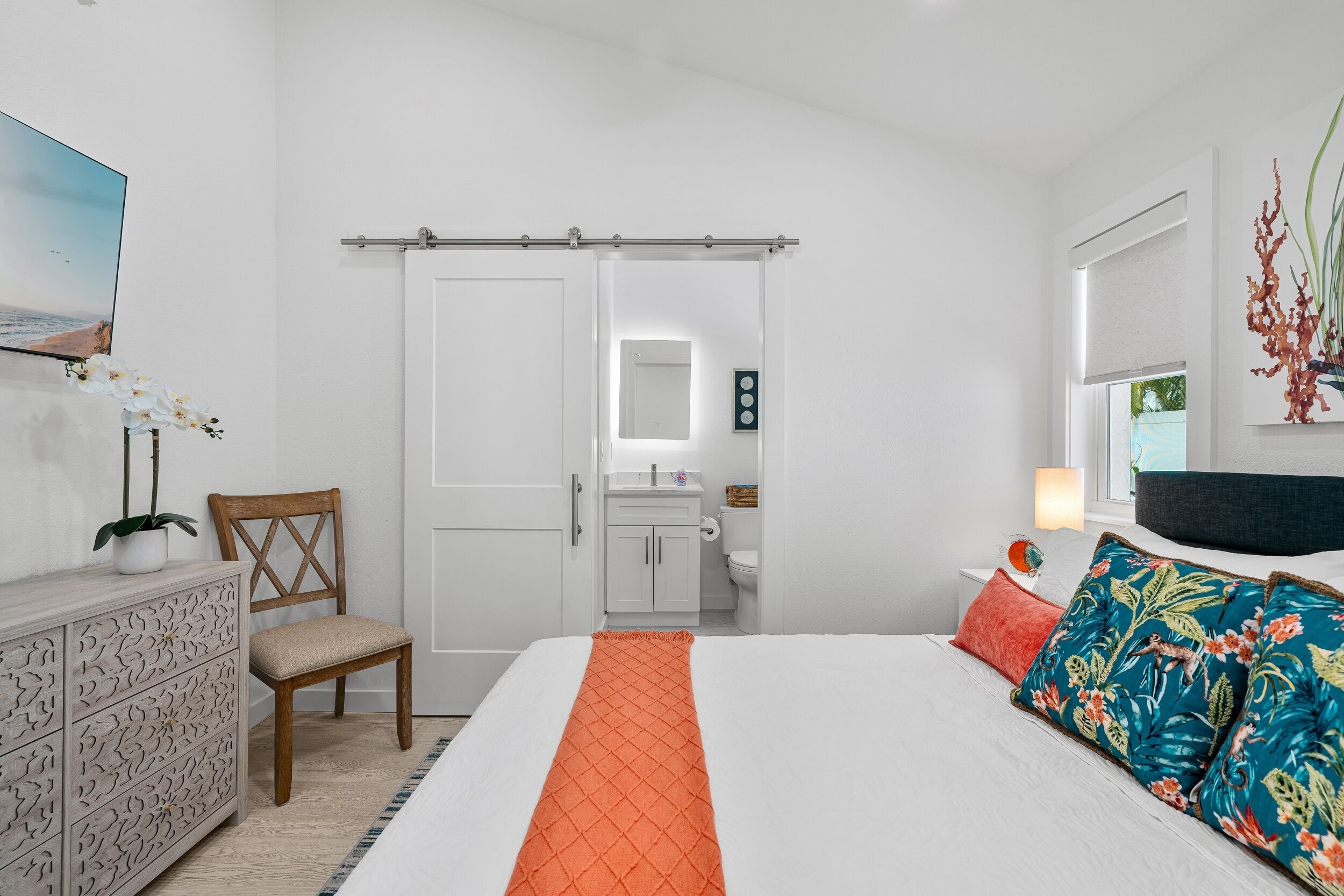 A bedroom with a bed, a chair, a dresser, a bathroom, and a door.