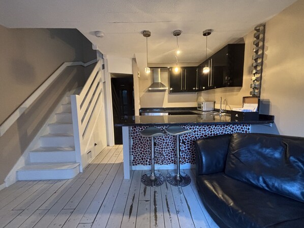 A modern kitchen with black cabinets, a central island, and a staircase leading to another level. - The Secluded Corner Wimbledon Chase With Parking (London)