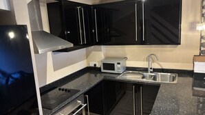 A modern kitchen with black cabinets, a stainless steel range hood, a microwave, and a sink. - The Secluded Corner Wimbledon Chase With Parking (London)