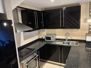 A modern kitchen with black cabinets, a stainless steel range hood, a microwave, and a sink. - The Secluded Corner Wimbledon Chase With Parking (London)