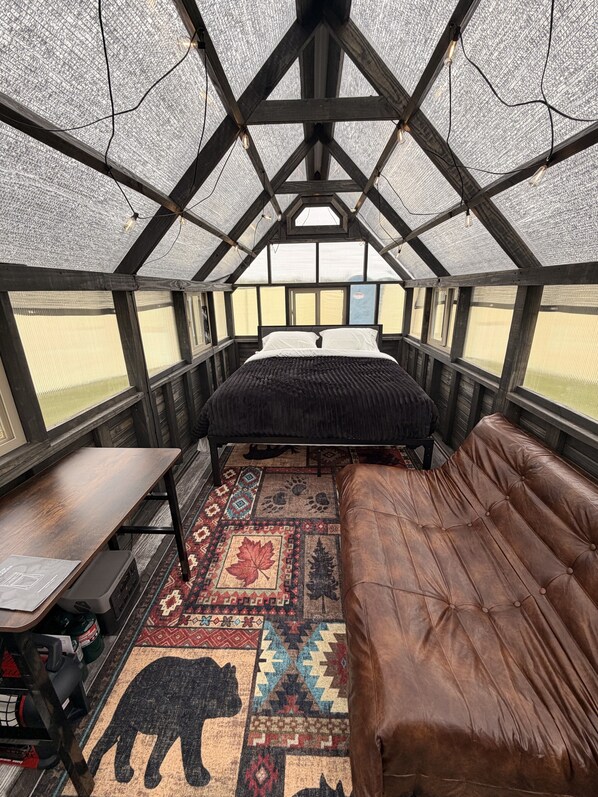 A high-ceilinged room with a bed, a leather couch, and a patterned rug.