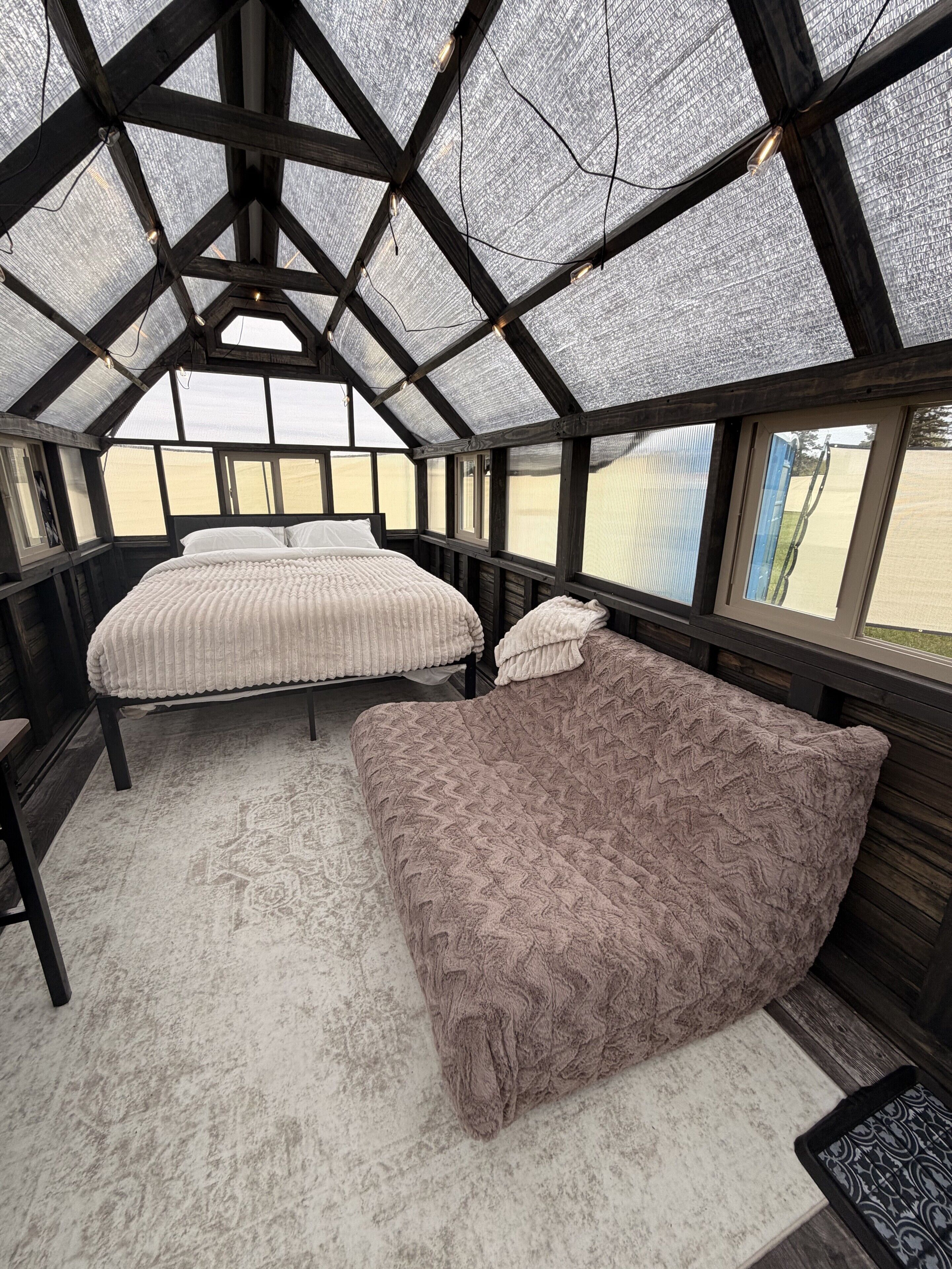 Una habitación con techo alto, vigas de madera, cama con colcha blanca y rosa, y un banco.