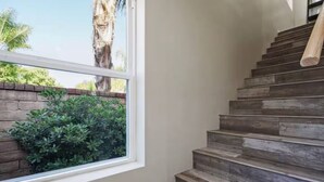 Un escalier en bois menant à un palier, une fenêtre donnant sur un paysage verdoyant et un mur de briques.