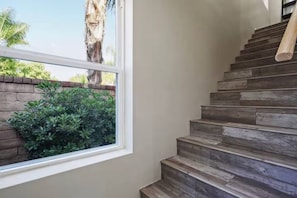 Un escalier en bois menant à un palier, une fenêtre donnant sur un paysage verdoyant et un mur de briques.