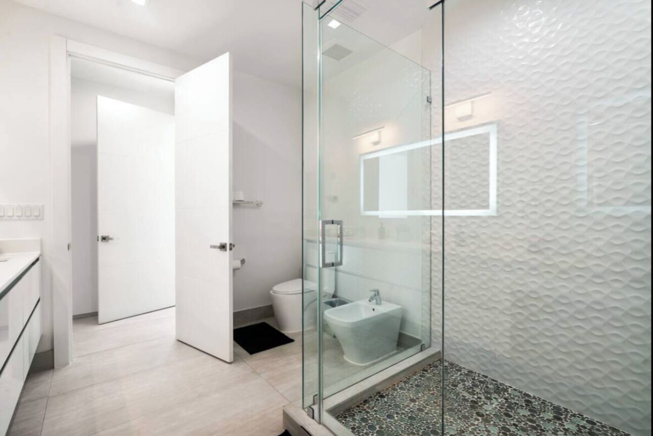 A modern bathroom with a glass shower enclosure, a white sink, and a textured wall.