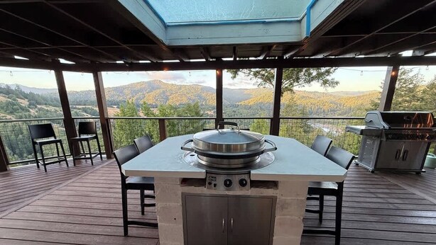 An outdoor deck with a built-in grill station, seating, and a view of the surrounding landscape.