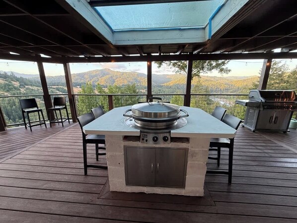 Une terrasse extérieure dotée d’un barbecue intégré, de coins salon et offrant une vue sur le paysage environnant.