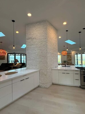 Une cuisine moderne avec des meubles blancs, un îlot central et des luminaires suspendus.