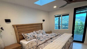 A bedroom with a bed, bedside tables, a ceiling fan, a skylight, and a window with a view.
