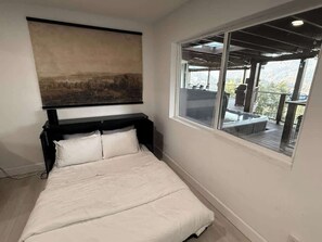 A bedroom with a bed, a large window, and a view of an outdoor deck.
