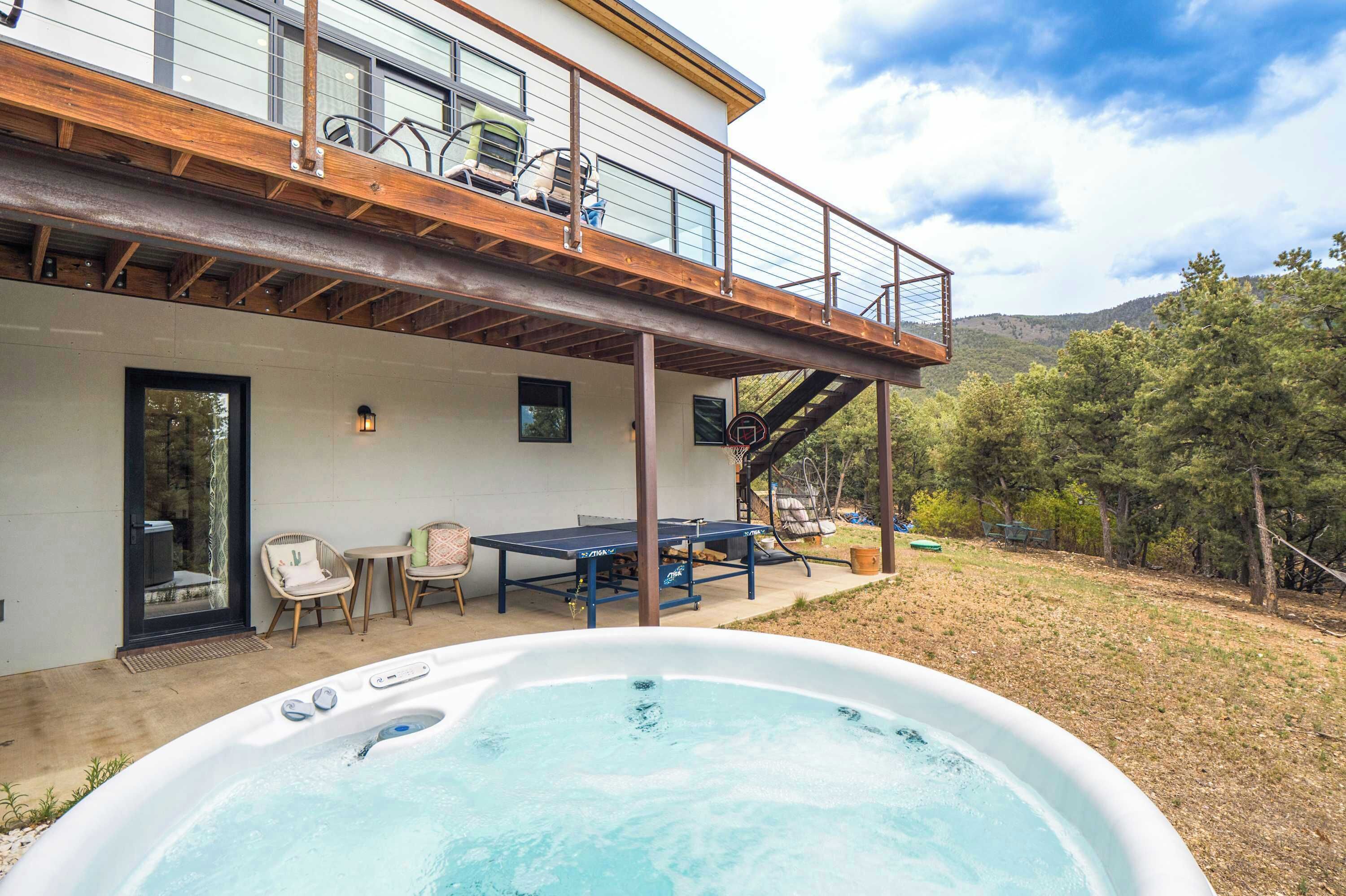 Un jacuzzi frente a una casa con balcón, mobiliario de exterior y un paisaje montañoso.