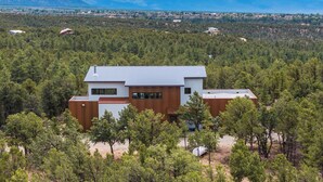 Una casa moderna rodeada de bosque frondoso, con vistas a montañas distantes.