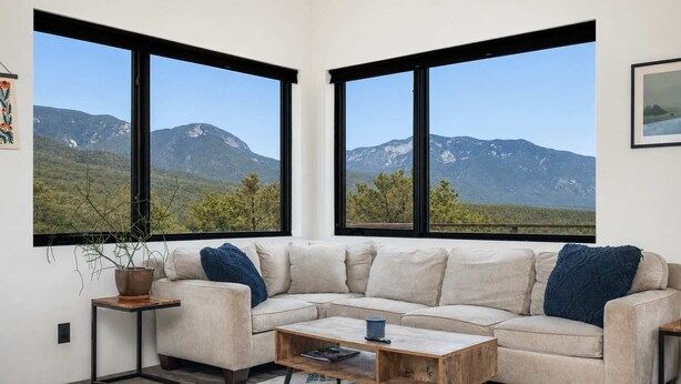 Una sala de estar con un sofá color beige, una mesa de centro de madera y vistas a montañas a través de ventanas amplias.