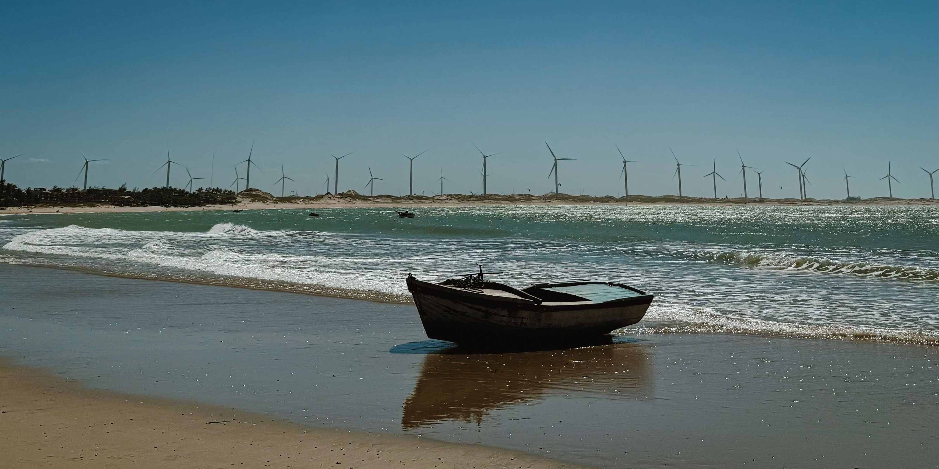 A boat on a beach with wind turbines in the background.