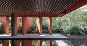 A modern architectural structure with a wooden slatted roof and a reflective water surface below.