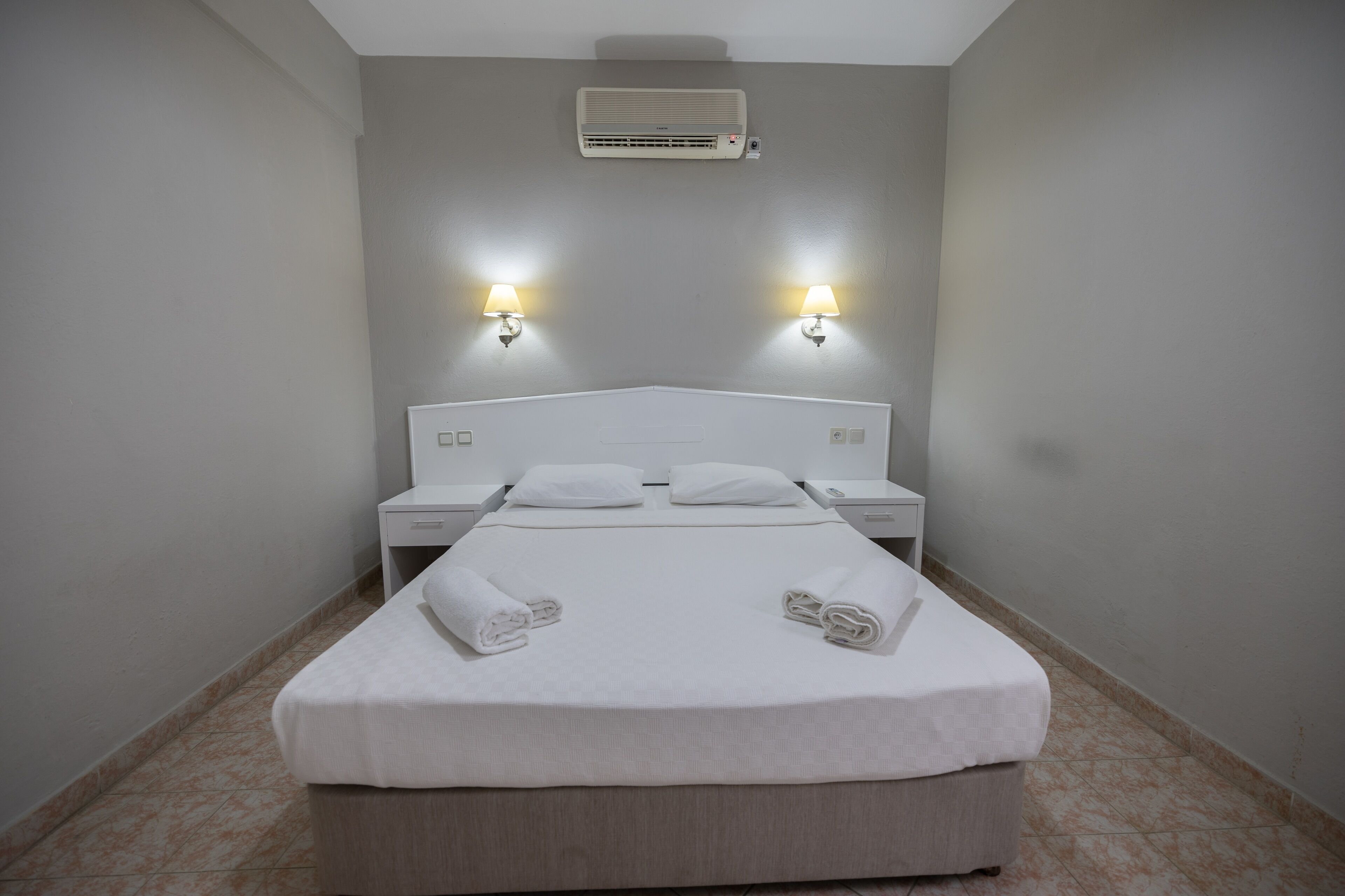 Habitación de hotel con cama, dos mesitas de noche, aire acondicionado y dos lámparas de pared.