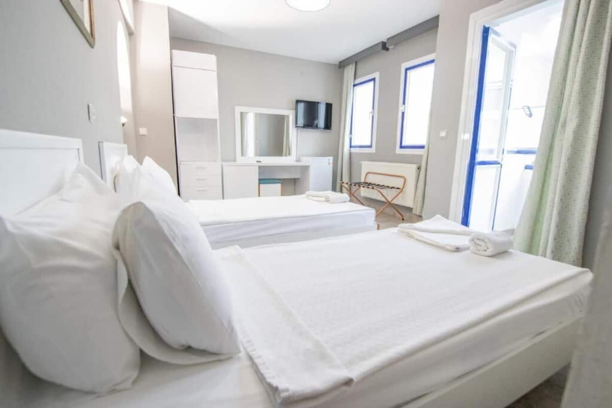 A hotel room with two beds, a TV, a mirror, a desk, and a window with curtains.